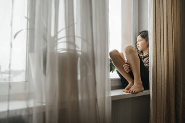 Trauriger Junge sitzt zu Hause auf der Fensterbank - ANAF01013