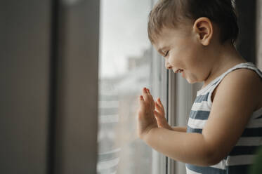 Glücklicher Junge schaut durch das Fenster zu Hause - ANAF01014