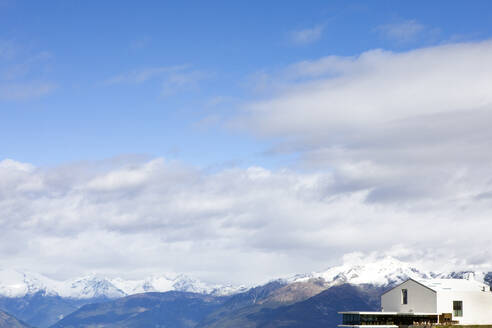 Kunstmuseum in der Nähe von schneebedeckten Bergen unter Wolken an einem sonnigen Tag - PSTF01045
