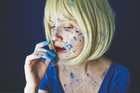 Woman with blue powder paint on face against blue background - SVCF00330