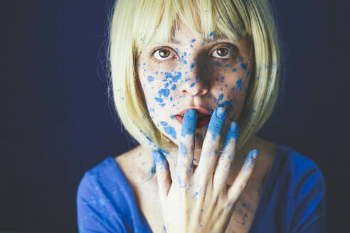 Blond woman with blue powder paint on face against blue background - SVCF00331