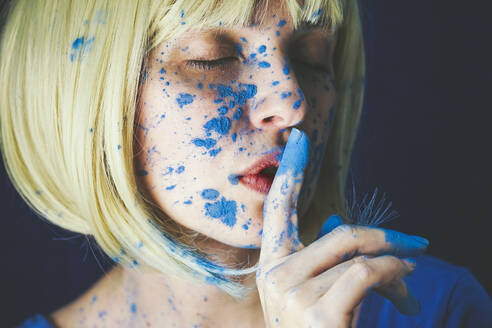 Frau mit blauer Puderfarbe und Finger auf den Lippen vor schwarzem Hintergrund - SVCF00334