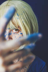 Blonde Frau schaut durch blau bemalte Finger - SVCF00339