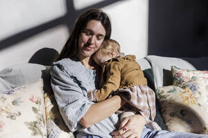 Mother with baby girl relaxing on sofa at home - RFTF00372