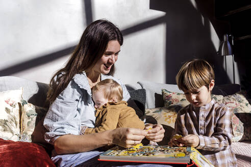 Lächelnde Mutter, die mit ihren Kindern zu Hause ein Puzzlespiel löst - RFTF00374