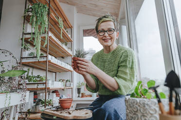 Smiling woman with succulent plant sitting by window at home - YTF00525