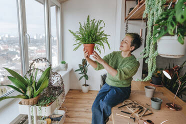 Lächelnde Frau betrachtet eine Farnpflanze zu Hause - YTF00528