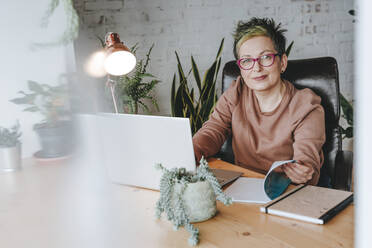 Reife Geschäftsfrau mit Brille sitzt am Schreibtisch im Home Office - YTF00537