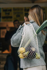 Woman carrying mesh bag with fruits and vegetables - VSNF00502