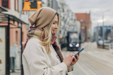Lächelnde Frau, die auf der Straße eine Textnachricht über ihr Smartphone verschickt - VSNF00514