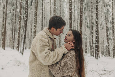 Romantic teenage couple standing together in snowy forest - VSNF00516