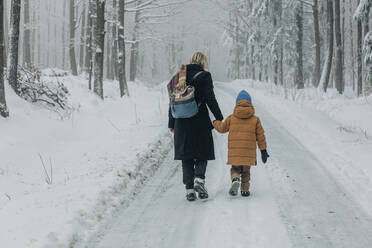Mother and son walking on footpath amidst snowy forest - VSNF00521
