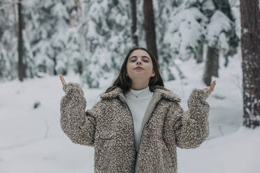 Teenager-Mädchen steht mit geschlossenen Augen im verschneiten Wald - VSNF00526