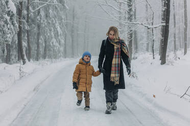 Mother walking with son on road in snowy forest - VSNF00527