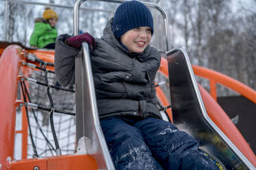 Junge spielt auf einer Rutsche auf einem Spielplatz im Winterpark - ANAF01015