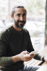 Lächelnder Mann mit Smartphone am Tisch im Café - JOSEF17163