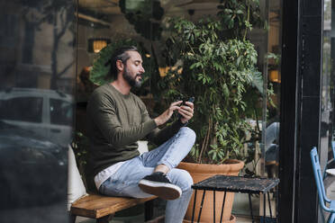 Älterer Mann mit Smartphone in einem Café sitzend - JOSEF17172