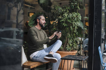 Mature man using smart phone sitting in cafe - JOSEF17172