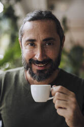 Smiling bearded man holding coffee cup in cafe - JOSEF17173