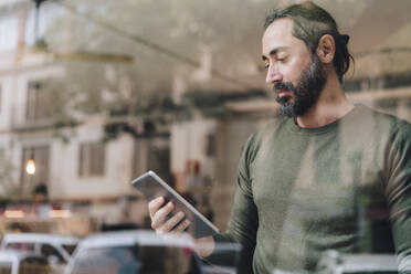 Mature man using tablet PC in cafe seen through glass - JOSEF17196