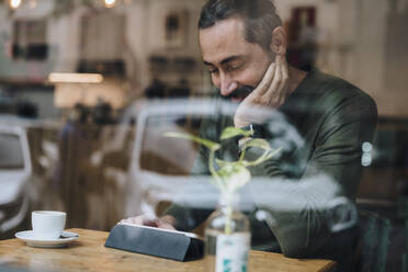 Smiling man watching videos on tablet PC in cafe - JOSEF17211