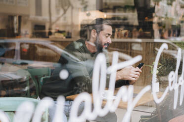 Mann benutzt Smartphone in Café durch Glas gesehen - JOSEF17213