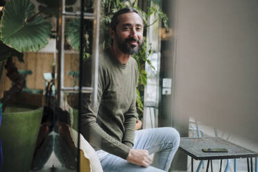 Smiling mature man with beard sitting in cafe - JOSEF17224