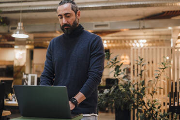 Älterer Geschäftsmann mit Laptop am Schreibtisch stehend bei der Arbeit im Büro - JOSEF17238