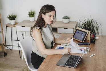 Businesswoman making notes from laptop in office - EBBF08044