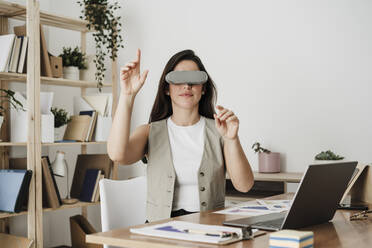 Geschäftsfrau mit Virtual-Reality-Simulator gestikuliert im Büro - EBBF08059
