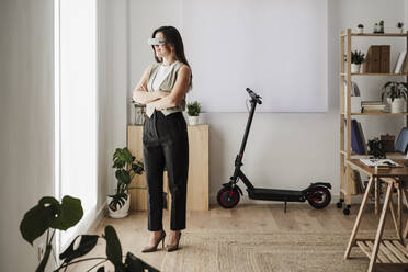 Geschäftsfrau mit VR-Brille steht mit verschränkten Armen im Büro - EBBF08065