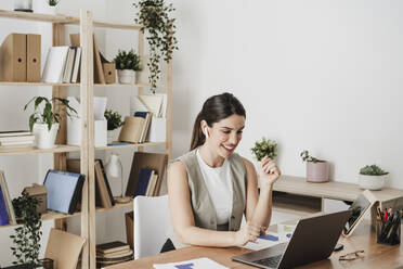 Happy businesswoman using laptop in office - EBBF08070