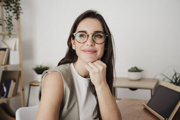 Thoughtful businesswoman with hand on chin sitting in office - EBBF08074