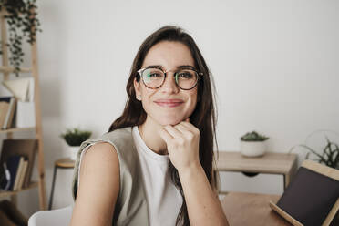 Smiling businesswoman wearing eyeglasses sitting in office - EBBF08075