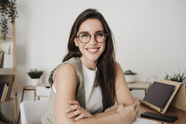 Happy businesswoman wearing eyeglasses at desk in office - EBBF08077
