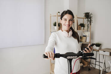 Happy businesswoman with electric scooter standing in office - EBBF08080