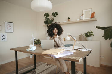 Thoughtful businesswoman sitting with laptop at desk in office - RCPF01658