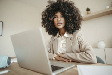 Selbstbewusste junge Geschäftsfrau mit Afrofrisur vor einem Laptop sitzend - RCPF01673