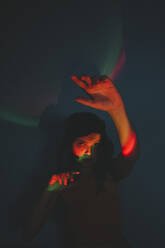 Woman with neon lights on face and raised hands in dark - SVCF00354