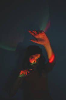 Frau mit Neonlicht im Gesicht und erhobenen Händen im Dunkeln - SVCF00354