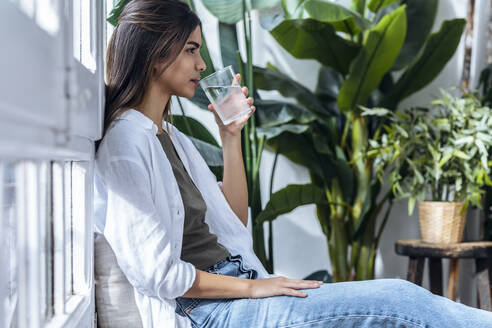 Young woman drinking water sitting by plants - JSRF02378