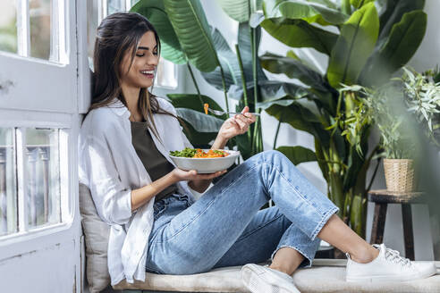 Happy woman eating salad at the window - JSRF02387