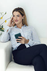 Smiling woman sitting with smart phone - JSRF02402