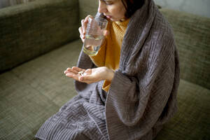 Kranke Frau, eingewickelt in eine Decke, nimmt zu Hause Medikamente ein - ANAF01017