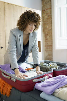 Frau bereitet Koffer für Reise im Schlafzimmer zu Hause vor - JSMF02663