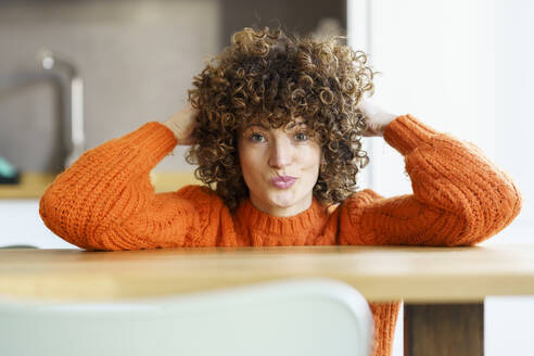 Woman with curly hair leaning at table in home - JSMF02675