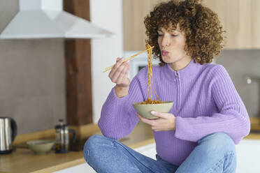 Woman with chopsticks eating noodles at home - JSMF02686