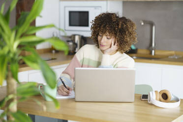 Freelancer writing on notepad at desk in home - JSMF02688