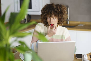 Freelancer eating raspberry and working on laptop at home - JSMF02689