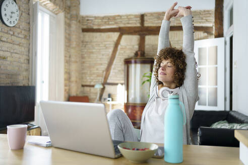 Freelancer stretching arms on desk at home - JSMF02695